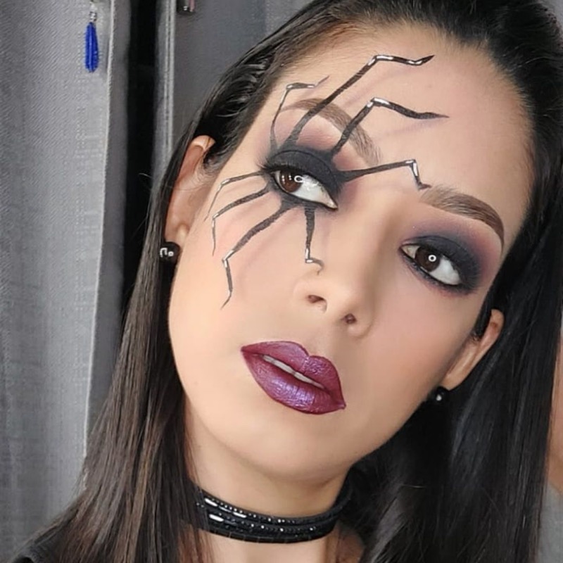 Maquillaje artístico editorial con diseño de araña en el ojo, sombras negras ahumadas y labios morado oscuro